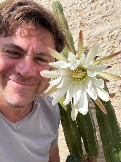 Man smiling next to a large white cactus flower.