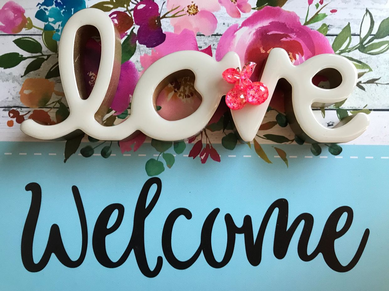 Decorative "love" sign with a pink butterfly on a floral welcome background.