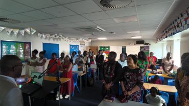 Group of people gathered in a classroom setting, listening attentively to a speaker.