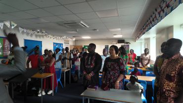 Group of people standing attentively in a decorated classroom.