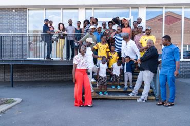 Large group of diverse people posing outside a building on stairs and balcony.