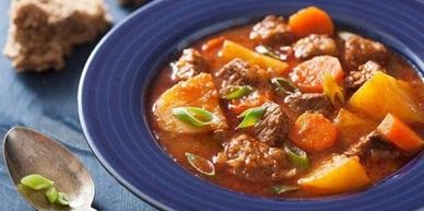 Hearty beef stew with carrots and potatoes in a blue bowl.