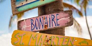 Colorful wooden signs pointing to Bonaire and St. Maarten on a beach.