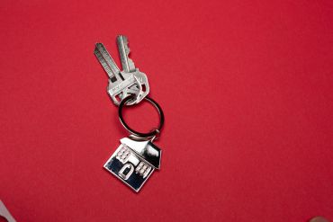 Two keys on a keyring with a house-shaped keychain against a red background.