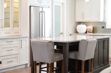Modern kitchen with white cabinets and a dark island with two upholstered chairs.