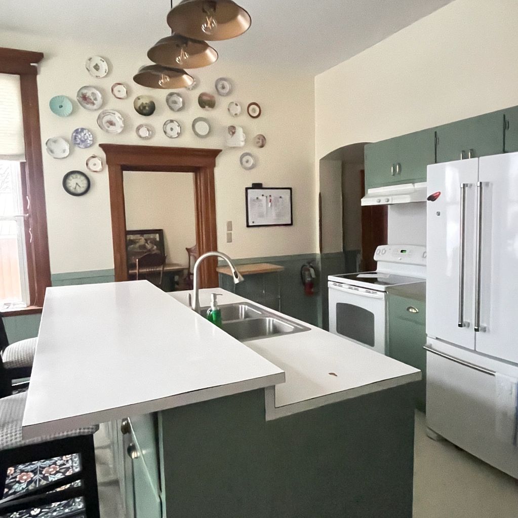 Bright kitchen with green cabinets, white countertops, and decorative plates on the wall.