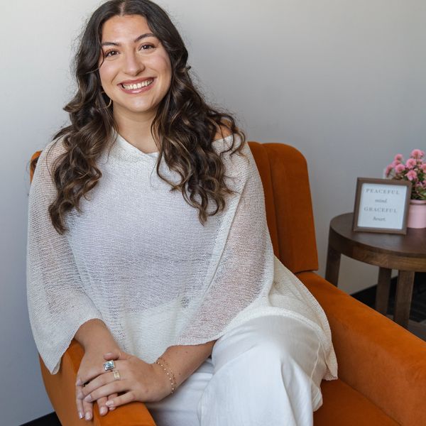 Smiling woman sitting on an orange chair in a cozy setting.