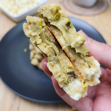 Close-up of a hand holding a green-frosted cookie with a crunchy center.