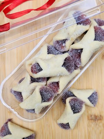 Homemade jam-filled sugar cookies in a plastic container on a wooden surface.