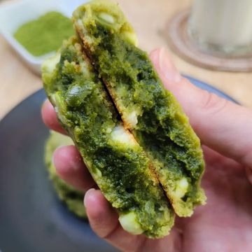 Hand holding a split green matcha-filled pastry with white chunks.