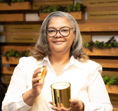 Woman holding a gold candle with a lid, smiling gently.