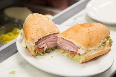 Ham sandwich with lettuce on a sesame roll, cut in half on a white plate.