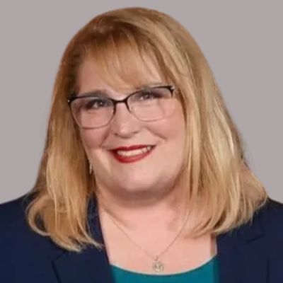 Professional woman with glasses smiling against a plain background.