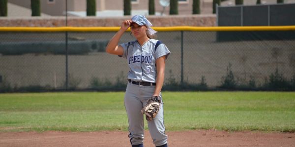 Softball player adjusting her cap on the field.