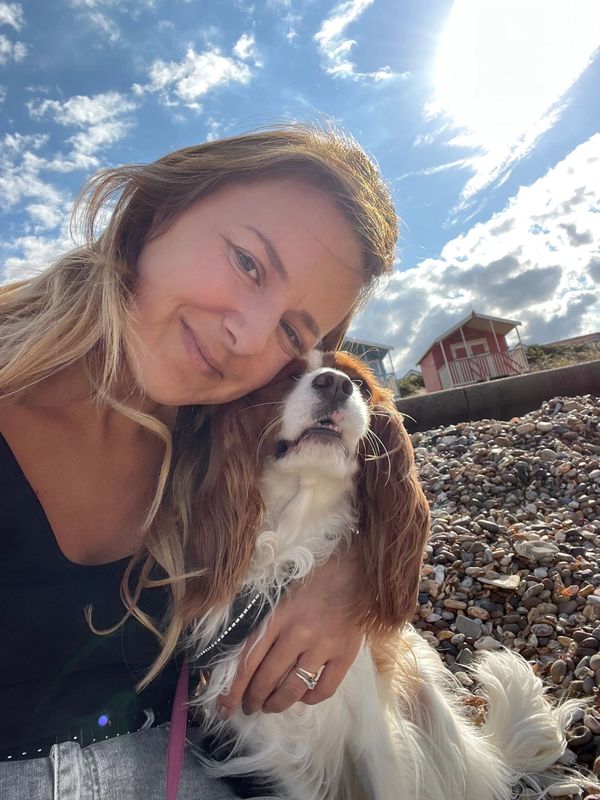 Woman smiling with her dog on a rocky beach under a partly cloudy sky.