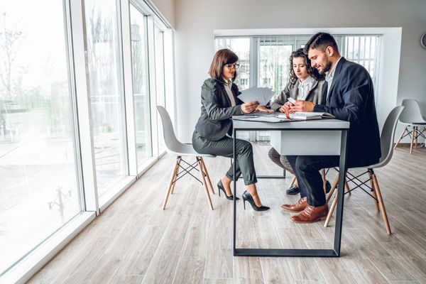 Real estate agent presenting property options to a couple in a modern office with large windows.