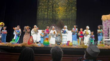 A group of people on stage holding colorful gourds in a forest-themed setting.