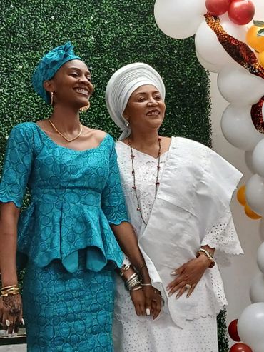 Two women dressed in traditional attire smiling and holding hands at an event.