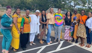 A diverse group of women standing outdoors, smiling and dressed in colorful, varied outfits.