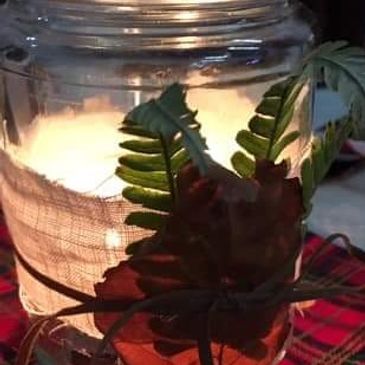 Glass container with green leaves and a glowing light inside.