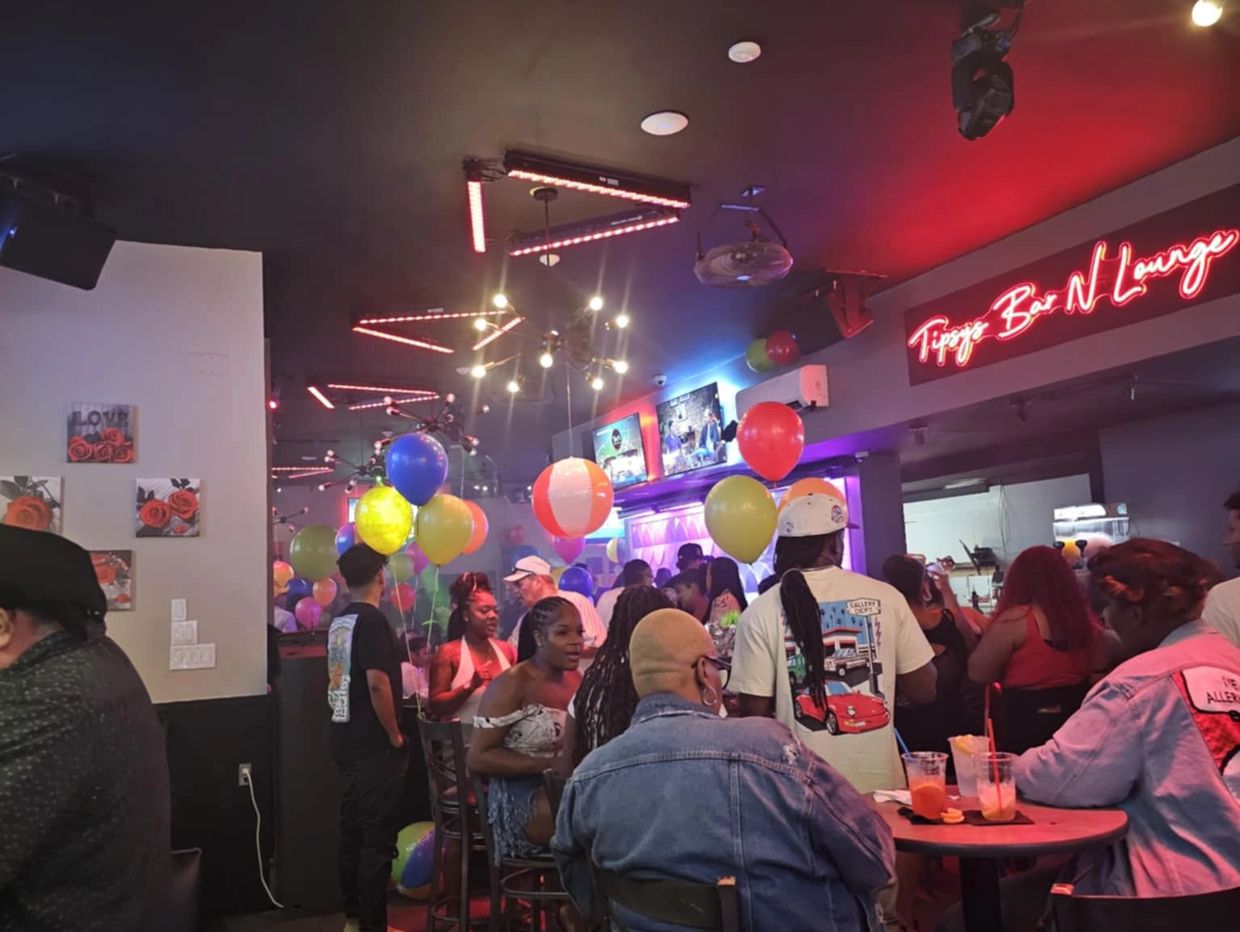 Packed crowd inside Tipsy’s Bar & Lounge with balloons, drinks, and neon red lighting.