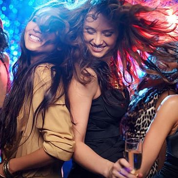 Group of women dancing, laughing, and having fun at a vibrant party with sparkling background lights.