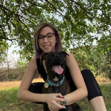 Suzie wrapping her arms around Bella while smiling; outside in a grassy area with surrounding trees