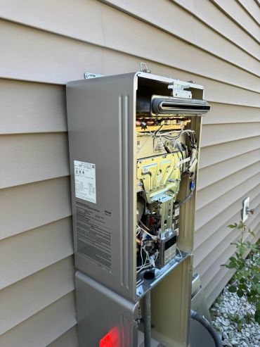 Outdoor tankless water heater with open panel showing internal components.