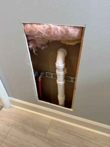 Wall cutout revealing plumbing pipes and insulation.