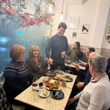 Group of people smiling and eating with the owner pouring a glass of wine.