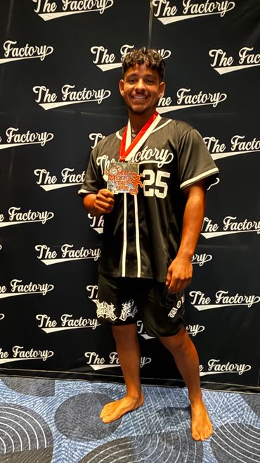 Young athlete proudly holding a medal in front of The Factory backdrop.