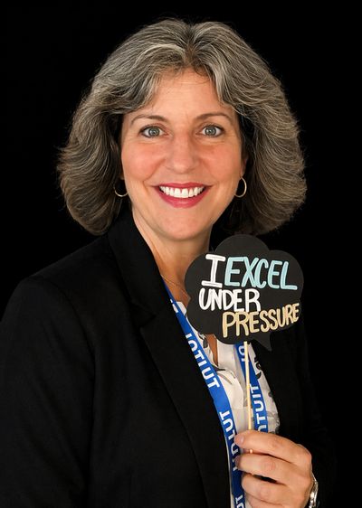 Woman holding a sign saying 'I Excel Under Pressure' with a bright smile.