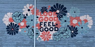 Colorful mural with flowers and the phrase 'Look Good Feel Good' on a blue brick wall.