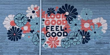 Colorful mural with flowers and the phrase 'Look Good Feel Good' on a blue brick wall.