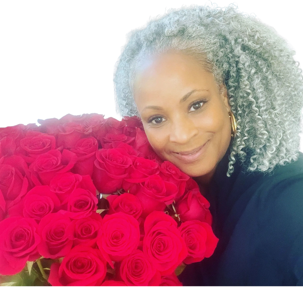 Smiling woman with curly gray hair holding a bouquet of red roses.