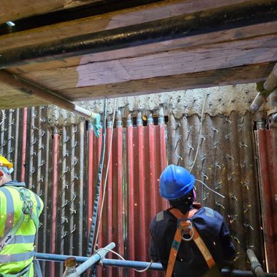 Construction workers inspecting a reinforced wall at a deep excavation site.
