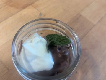 A glass jar with chocolate mousse, whipped cream, and a mint leaf on top.