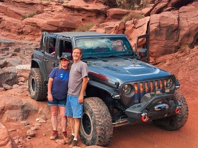 Couple posing next to a black Jeep Wrangler on a rocky trail.