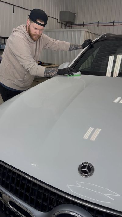 Man wearing gloves detailing a white Mercedes car indoors.