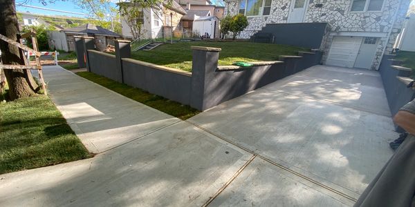 A clean driveway and sidewalk with a small lawn and stone-patterned house.