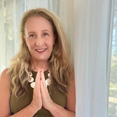 Woman with long hair in a green dress, hands pressed together in a peaceful gesture.
