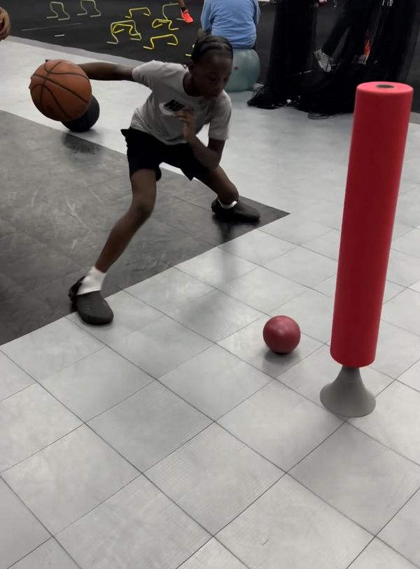 Young boy dribbling a basketball during a training drill indoors.