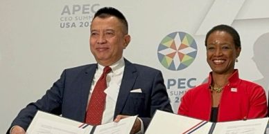 Two professionals smiling while holding documents at the APEC CEO Summit.