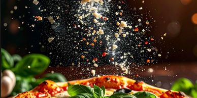Pizza topped with fresh basil and falling grated cheese.