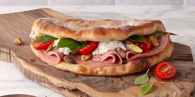 A fresh sandwich with ham, mozzarella, tomatoes, and greens on rustic bread.