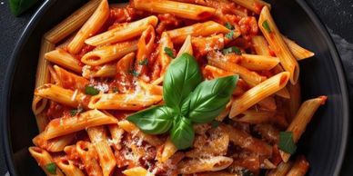 Plate of penne pasta with tomato sauce and basil garnish.