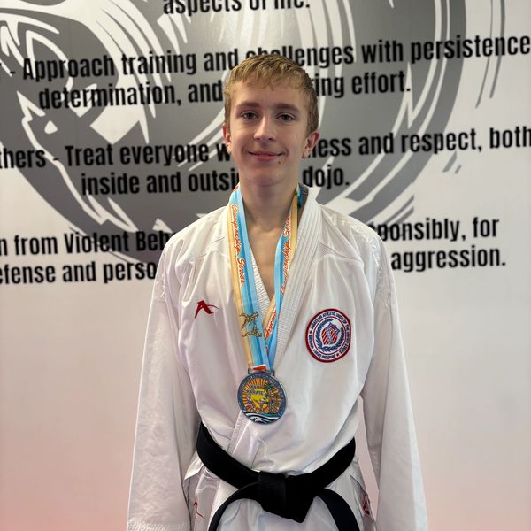 Young martial artist proudly wearing a medal and black belt.