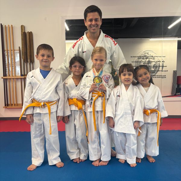 Kids in karate uniforms with yellow belts and their instructor posing for a photo.