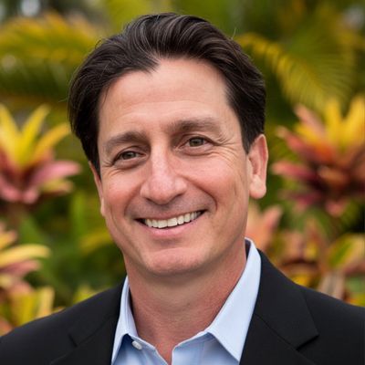 Smiling man in a suit with a tropical background.