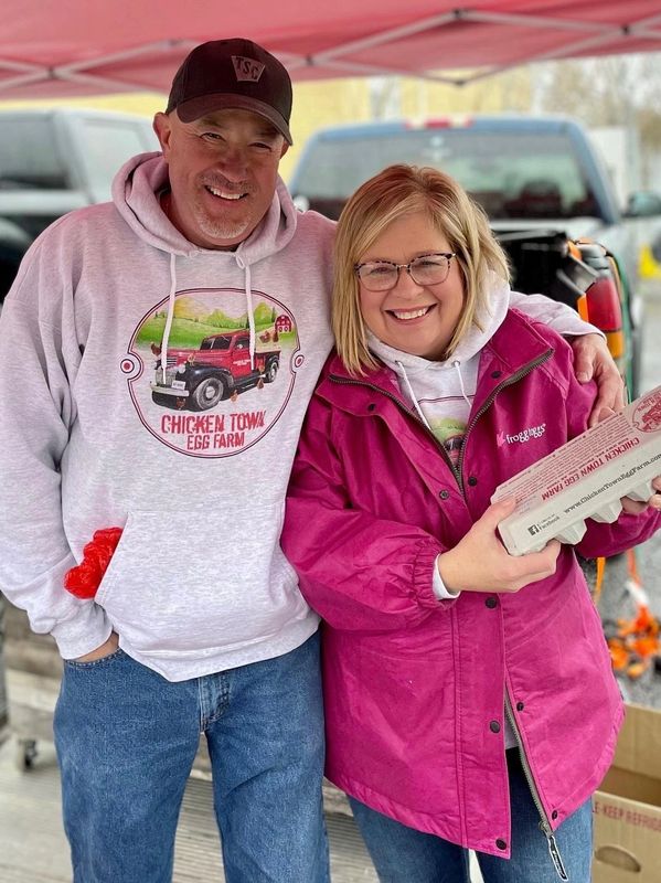 A man wearing a Chicken Town Egg Farm logo hoodie and a woman in a pink jacket holding an egg carton